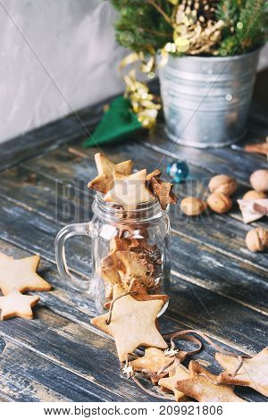 Homemade shortbread star shape sugar cookies different size in glass jar and as garland on old wooden table decorated by Christmas tree and gifts. Christmas mood theme. Toned image.