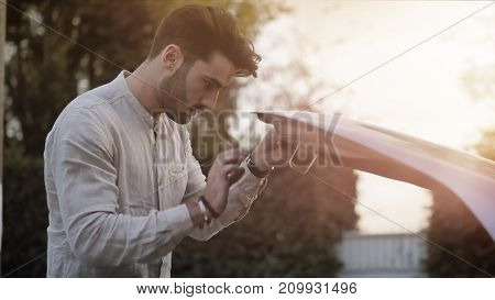 Handsome young man trying to repair a car engine, looking inside open bonnet
