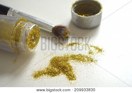 Sequins of gold color scattered on a white background and a black brush for their application