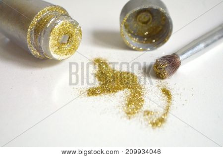 Sequins of gold color scattered on a white background and a black brush for their application