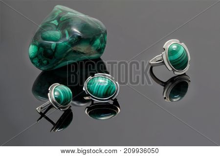 Closeup beauty silver earrings and ring with malachite on background of malachite stone piece on black acrylic desk.