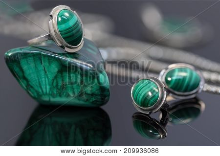 Closeup vintage silver earrings and ring with malachite on top of malachite stone piece on background of silver chain on black acrylic desk.