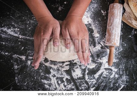 Male hands kneading dough sprinkled with flour table Hands preparing bread Raw dough for bread with ingredients on black background.