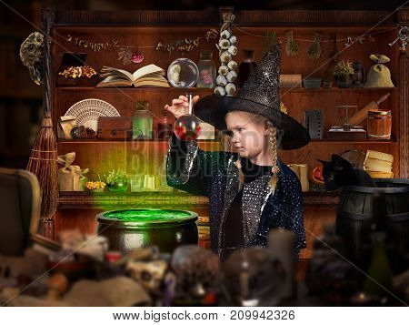 Room wizard. The little girl in the witch hat looking for the magic elixir in the retort. Many mystical items. The concept of magic Halloween