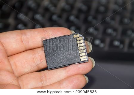 Hand holding SD card on laptop background