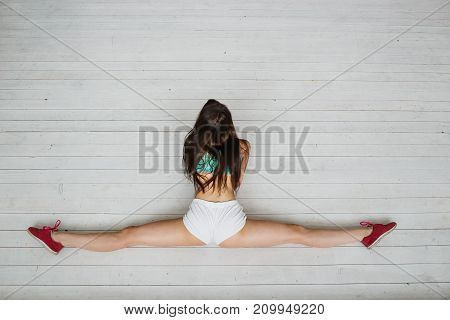 Flexible latina girl doing stretching exercise for legs. Young woman stretches out on white floor. Top view with copyspace.