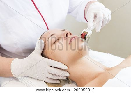 The woman undergoes the procedure of medical micro needle therapy with a modern medical instrument derma roller.