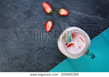 A top view on a mason jar with tasty fresh jogurt and three pieces of strawberries on a marble background. Close-up of drink. Food concept.