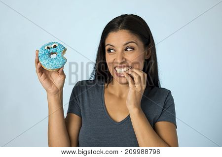 young happy attractive Latin woman smiling excited holding sugar donut isolated on blue background in sugar abuse nutrition and diet health care concept surrendering to temptation
