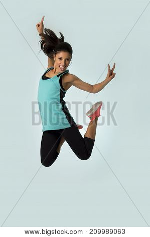 young attractive and happy Latin sport woman jumping excited and cheerful in gym exercise workout healthy lifestyle and freedom concept isolated on clear background with studio light
