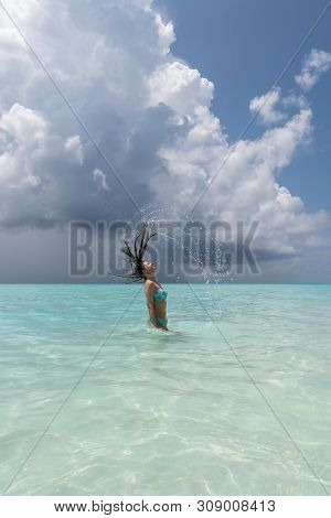 A Young Girl Makes Splashes When She Drastically Pulls Her Hair Out Of The Water.