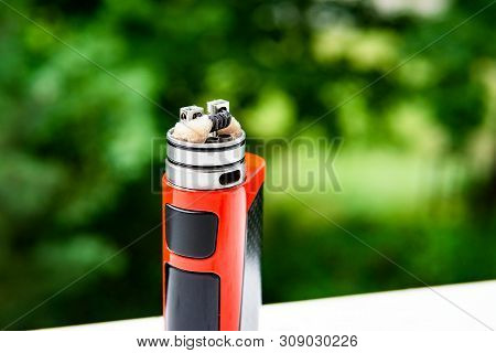 Electronic Cigarette On The Background Of Trees, Visible Spiral Wool And Steam. Coil Cleaning.