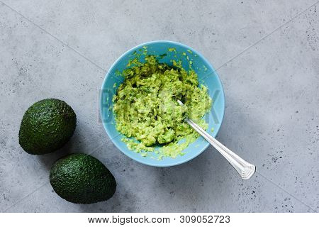 Mashed Avocado In Bowl On Grey Concrete Background. Table Top View. Cooking Healthy Vegan Or Vegetar