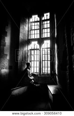 Rear View At Silhouette Of Man Sitting In The Darkness Looking Through Old Bright Window With Incomi