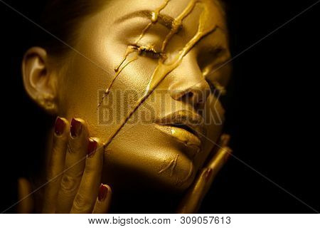 Gold Paint smudges drips from the face lips and hand, lipgloss dripping from sexy lips, golden liquid drops on beautiful model girl's mouth, gold metallic skin make-up. Beauty woman makeup close up.