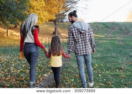 Fall Family Leisure. Back View Of Parents Walking With Daughter In Nature Park. Trees, Faded Grass, 