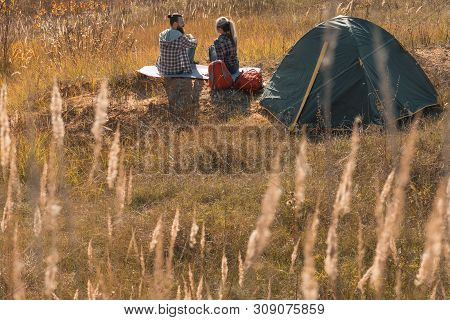 Romantic Camping. Back View Of Couple Sitting On Ground, Talking. Tent, Fall Nature Background.
