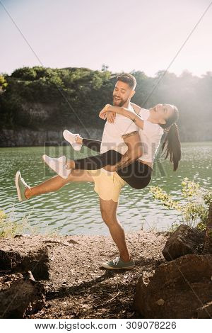 Young Couple Having Fun At Riverside In Sunny Day. Woman And Man Spending Time On The Nature Togethe