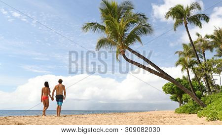 Beach summer vacation couple walking under palm trees in bikini and swim trunks.