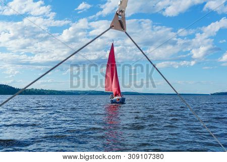 Small Yacht With Scarlet Sails Sailing Around The Bay, Visible From The Board Of Another Boat Throug