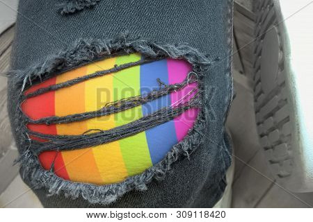 Hole And Threads On Denim Jeans Surface With Lgbt Pattern. Young Fashion Man's Legs In Jeans.