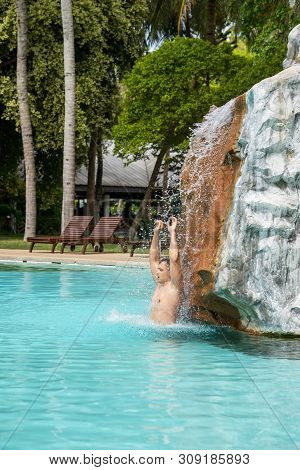 A Young Guy Stands Under Artificial Waterfalls In The Pool On Site