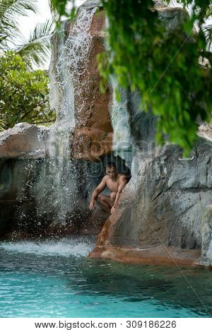 A Young Guy Sits In A Rock Behind A Waterfall