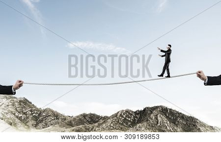 Businessman Walking Blindfolded On Rope Above High Mountains As Symbol Of Hidden Threats And Support