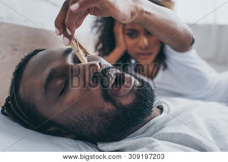Selective Focus Of Snoring African American Man Near Wife Holding Wooden Pin