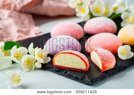 Multi-colored Japanese Ice Cream Mochi In Rice Dough And Jasmine Flowers On A Concrete Blue Backgrou