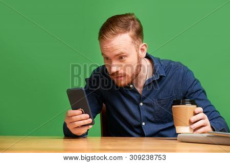Amazed Young Man With Cup Of Take Away Coffee Reading Shocking News On Smartphne Screen