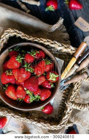 Overhead Shot Of Tasty Ripe Strawberries In Wooden Bowl Stands In Wicker Strawy Basket On Rustic Tab