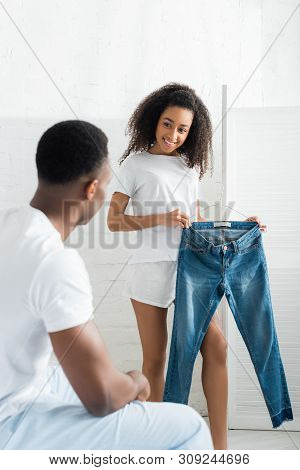 Selective Focus Of Happy African American Woman Showing Denim Jeand Pants To Boyfriend