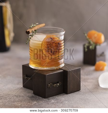 Whiskey sour cocktail with tangerine slices and ice cubes decorated with cinnamon and thyme. Alcohol