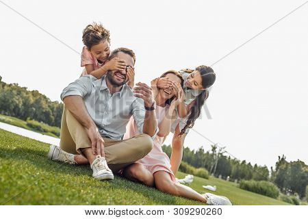 Guess Who Happy Young Family Of Four Smilin And Having Fun While Sitting On Grass In Park
