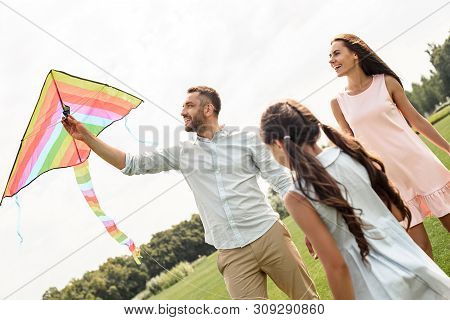 Feeling Happy Active Parents And Child Daughter Launcing A Kite In The Field.