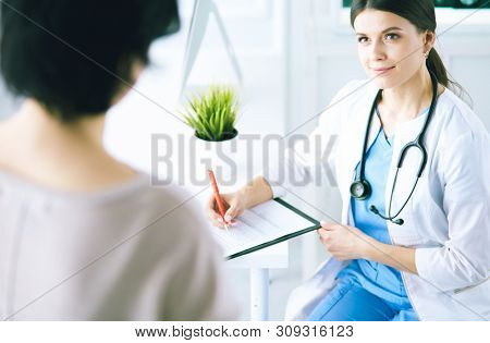 Doctor and patient discussing medical problems in a hospital consulting room. Doc filling in a patient's form