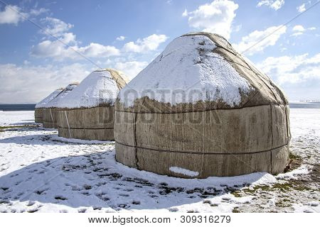 Yurts Under The Snow In The Middle Of A Snow-covered Field Against A Sky With Clouds. Travel Kyrgyzs