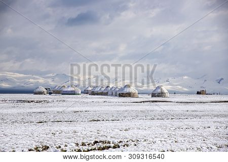 Yurt Town On A Snowy Pasture On The Background Of Snow-capped Mountains And Sky With Clouds. Son-kul