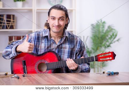 Young handsome repairman repairing guitar