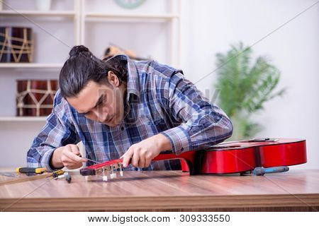 Young handsome repairman repairing guitar