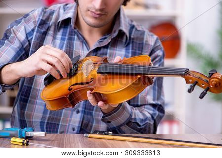 Young handsome repairman repairing violin