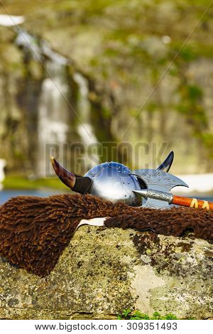 Equipment Of Viking Or Barbarian Warrior Outdoor On Nature. Viking Helmet With Axe On Brown Fur Of T
