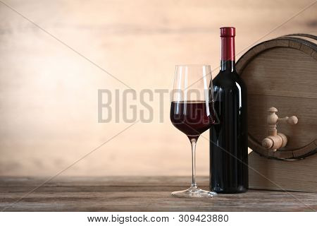 Glass And Bottle Of Red Wine Near Wooden Barrel On Table. Space For Text