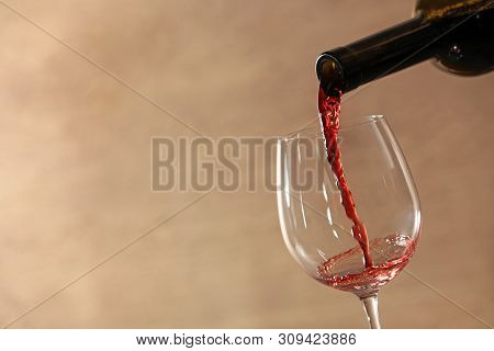 Pouring Red Wine Into Glass From Bottle Against Blurred Beige Background, Closeup. Space For Text