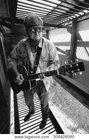 Bluesman With Acoustic Guitar In Grayscale. Cool Guy Plays Guitar. Performance Of Wandering Blues Mu