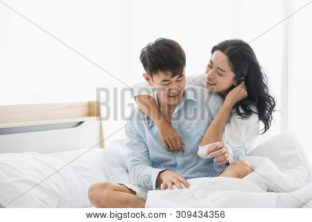 Asian Couple Sitting On The Bed Together, Woman Blindfolded Boyfriend.