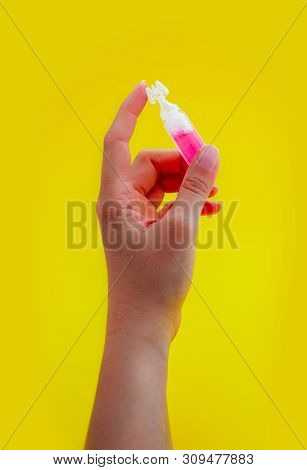Female Hand Holding One Pink Liquid Medicine In An Ampoule, Isolated On Yellow Background.