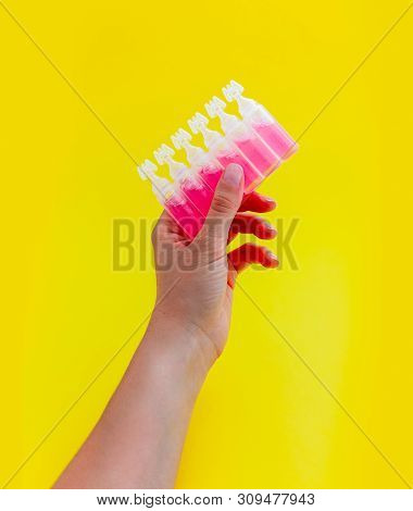 Female Hand Holding Ampoules With Pink Liquid Medicine, Isolated On Yellow Background.