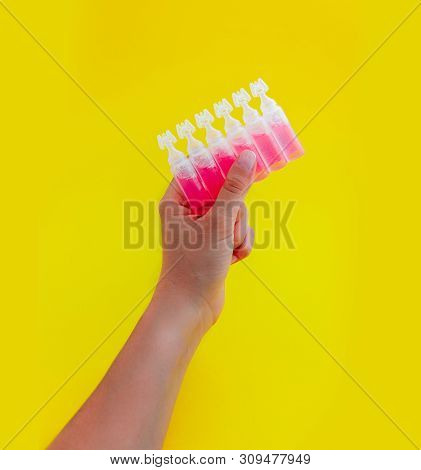 Female Hand Holding Ampoules With Pink Liquid Medicine, Isolated On Yellow Background.